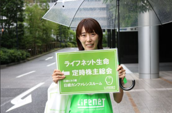 第18回定時株主総会（2024年6月23日）の案内カードを持つ女性の写真